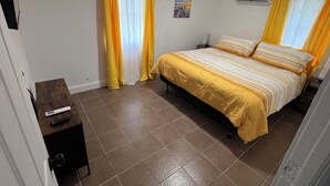 A bedroom with a bed, curtains, a nightstand, a remote control, and an air conditioning unit. - Space Coast getaway! The Yellow Sunrise! 2 bed 1 bath Oasis (Merritt Island)