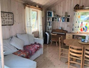 Una cabana amb un sofà, una taula de menjador amb cadires, una estanteria i un piano.