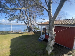 Una cabana a la vora d'un llac amb un porxo, façana vermella i vistes a l'aigua.