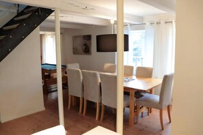 Ein Essbereich mit einem Holztisch, sechs Stühlen, einer Treppe und einer Wandlampe.