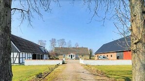 Ein ländliches Anwesen mit einem Schotterweg, der zu einem zentralen Gebäude führt, das von zwei Scheunen gesäumt wird.