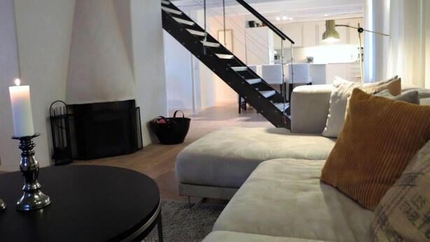 Ein modernes Wohnzimmer mit einer Couch, einem Tisch mit Kerze, einem Kamin und einer Treppe zu einem anderen Raum.