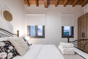 Ein Schlafzimmer mit einem Bett, zwei Fenstern, einer Holzbalkendecke und einem Kleiderschrank.