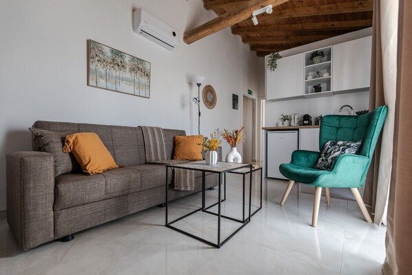 Ein Wohnzimmer mit grauem Sofa, einem Türkis-Armlehnstuhl, einem Couchtisch und einer Küche im Hintergrund.