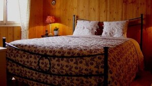 Una cama con colcha estampada floral, una mesita de noche con lámpara y una pared de madera.