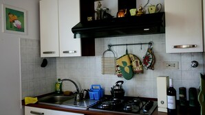 Una cocina con gabinetes blancos, estufa, pileta y diferentes utensilios de cocina.