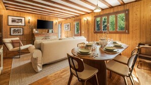 Un interior de madera con una mesa de comedor preparada para cuatro, un sofá y un televisor montado en la pared.