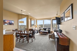A spacious living area with a dining table, chairs, a sofa, and a coffee table. Large windows offer a view of the outdoors. - New Listing! River Views | Hot Tub | Near Mt. Bachelor (Bend)