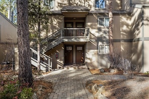 A building with a central entrance, a staircase leading to a balcony, and a paved pathway. - New! Remodeled Condo | Pool - Hot Tub | Steps to River Trail (Bend)