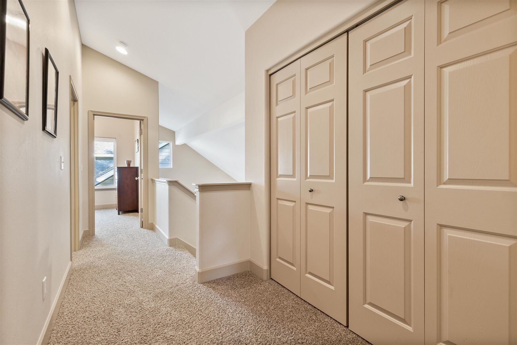 A hallway with carpeted flooring, a staircase, and beige double doors.