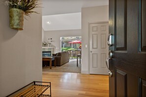 Ein Flur, der zu einem Essbereich mit Holzboden führt, mit einer weißen Tür mit modernem Griff und einer Zimmerpflanze an der Wand.