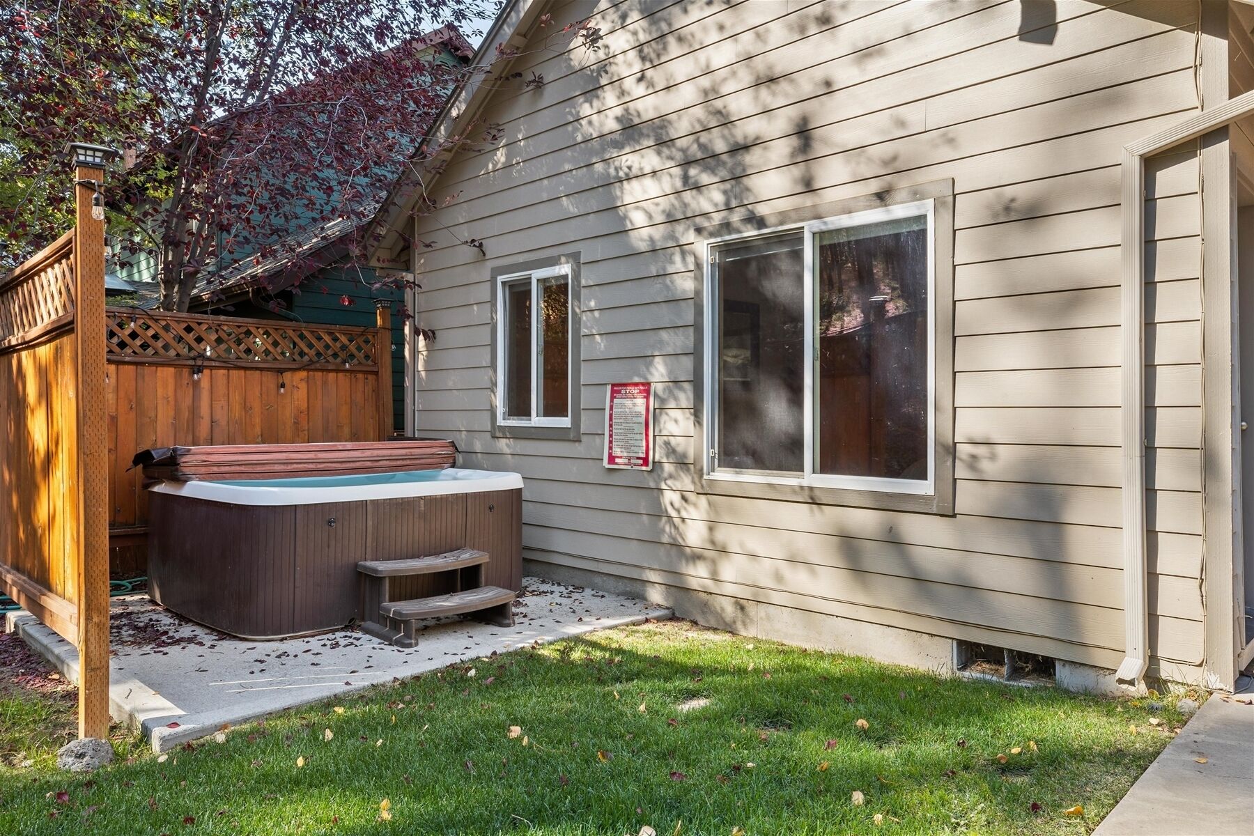 A wooden house with a hot tub, a wooden deck, and a fenced yard.