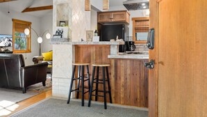 Eine Küche mit Holzausstattung, einem schwarzen Kühlschrank und einer Kaffeemaschine. Zwei Barhocker und eine Holzelemente-Bar sind ebenfalls vorhanden.