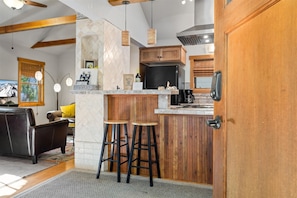 Eine Küche mit Holzausstattung, einem schwarzen Kühlschrank und einer Kaffeemaschine. Zwei Barhocker und eine Holzelemente-Bar sind ebenfalls vorhanden.