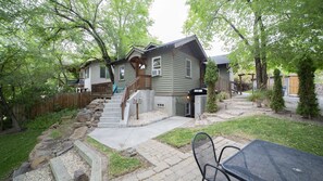 Une maison à deux étages avec un porche à l’avant, un escalier et une cour arrière comprenant une table et des chaises de patio.
