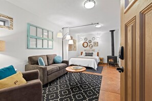 Ein gemütliches Zimmer mit einer Couch, einem kleinen Tisch, einem Bett mit Kopfteil, einem an der Wand befestigten Spiegel und einem Kaminofen.