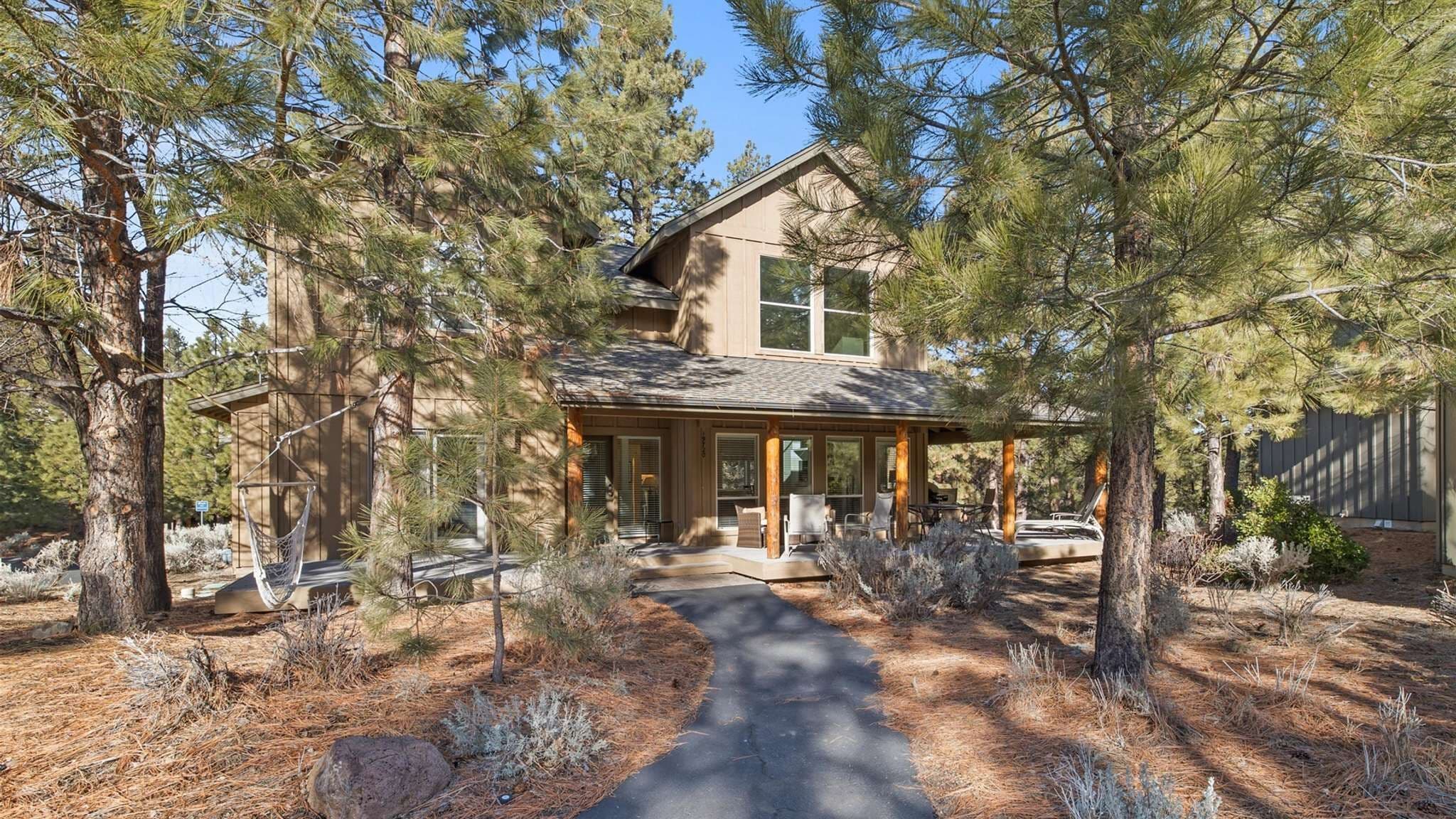 Una casa de dos pisos con porche cubierto, rodeada de pinos.