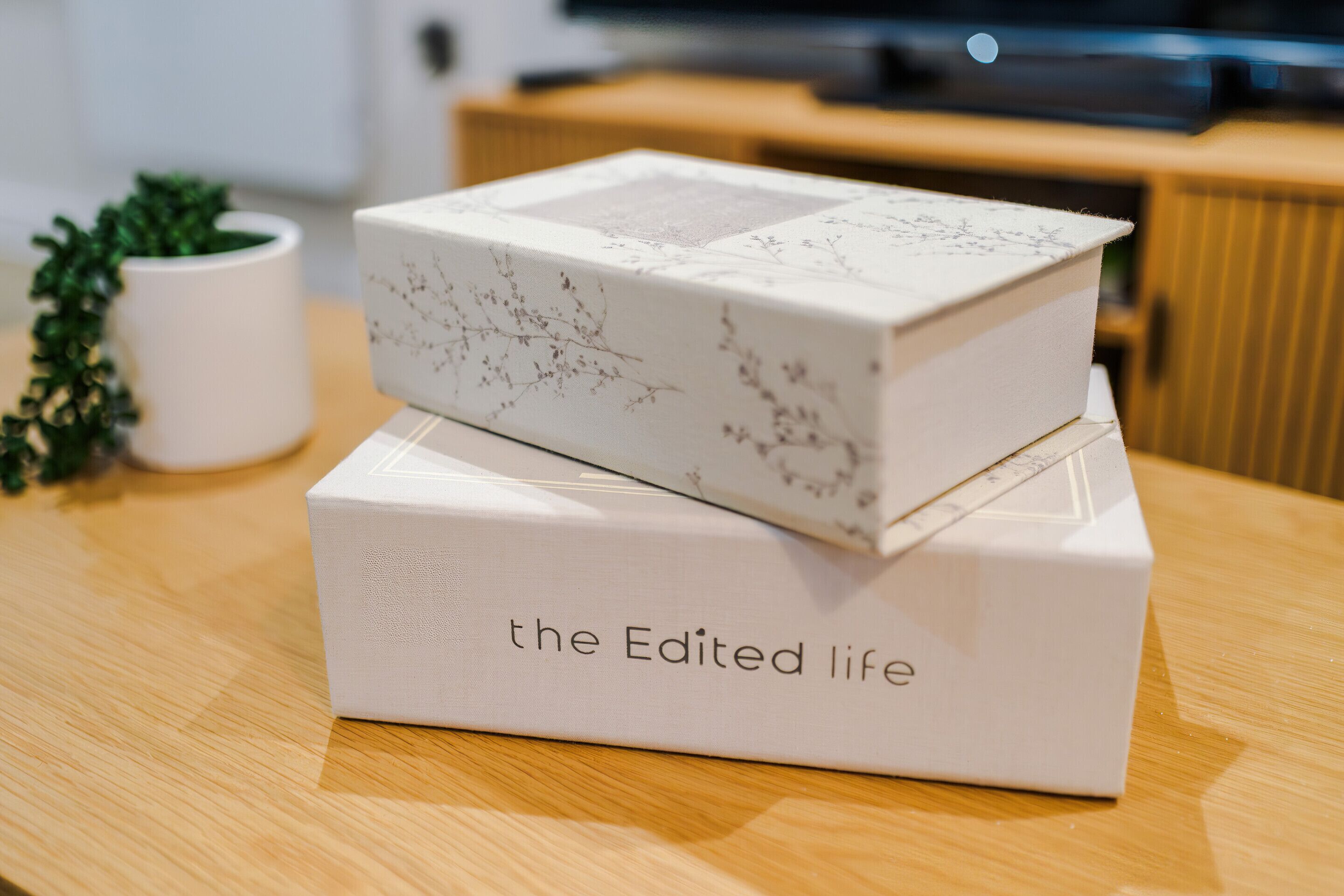 Two white boxes with floral patterns and text on a wooden table.