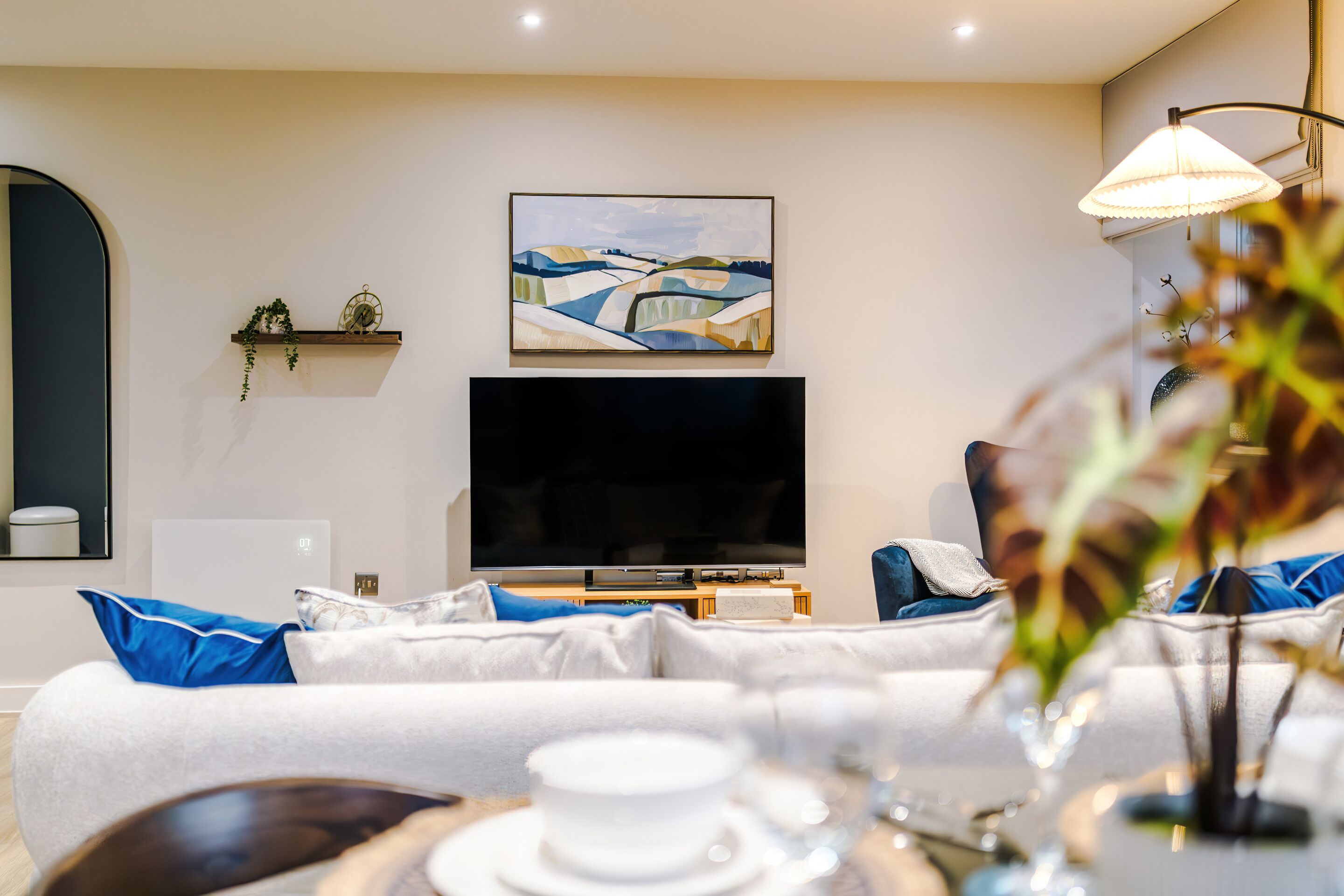 A modern living room with a flat-screen TV, a sofa with blue cushions, a coffee table, and a painting on the wall.