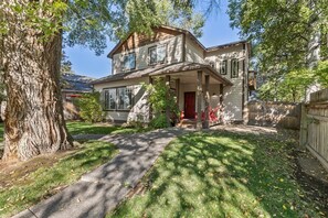 Ein zweistöckiges Haus mit einer Veranda, einer roten Tür und einem großen Baum im Vorgarten.