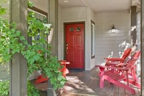 Eine Veranda mit roter Tür, zwei roten Adirondack-Stühlen und einem Blumentopf.