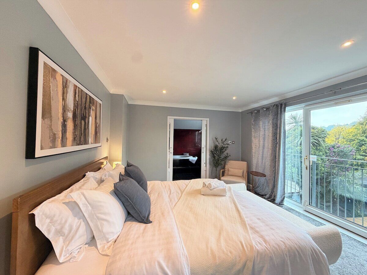 A hotel room with a large bed, a painting on the wall, a chair, and a balcony with a view.