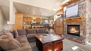 Ein modernes Wohnzimmer mit einem Ecksofa, einem Kamin und einer Küche im Hintergrund.