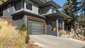 A modern two-story house with a garage, large windows, and a well-maintained front yard. - New! Modern Bend Retreat | Views | Hot Tub | Fenced Yard (Bend)