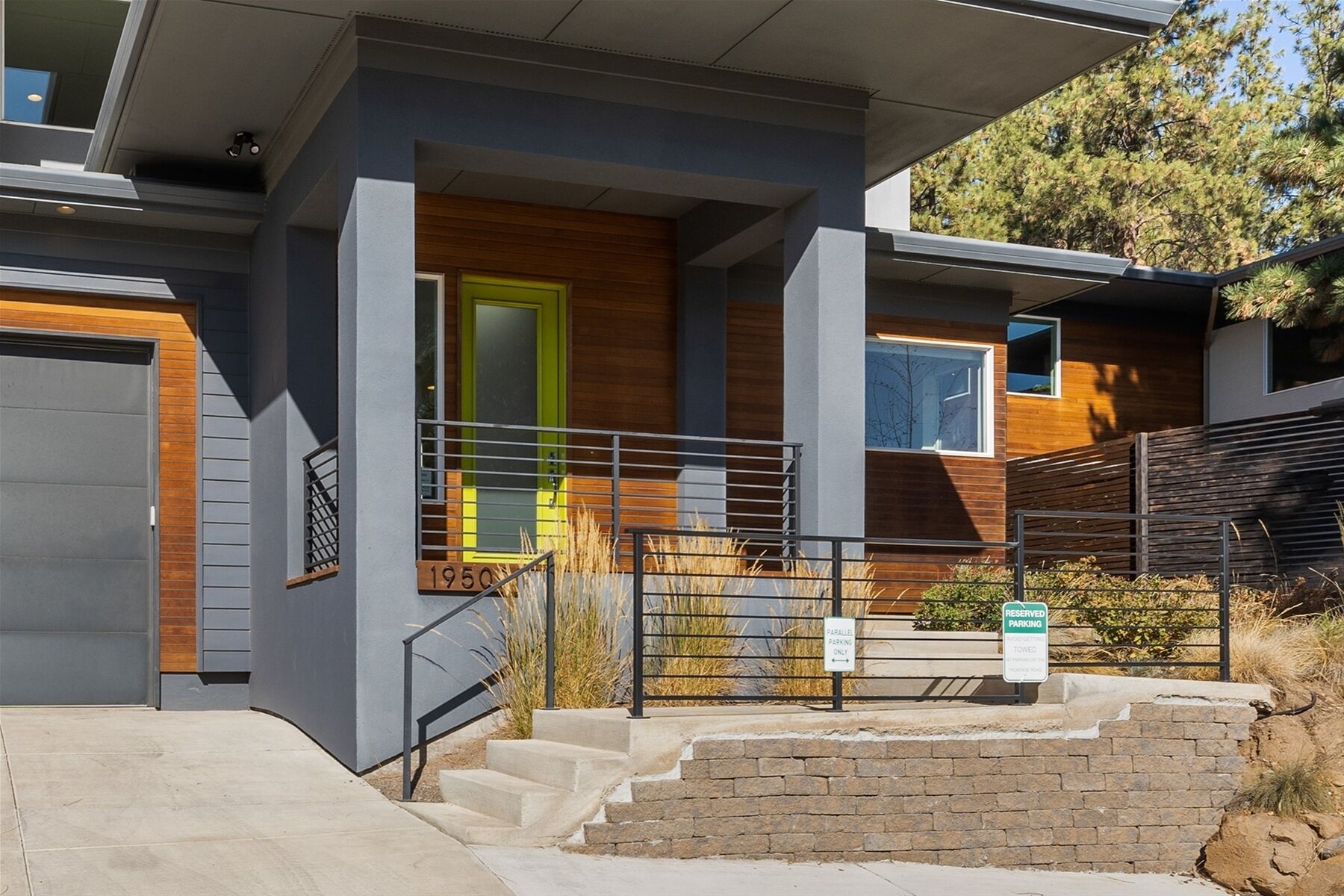 A modern two-story house with a grey exterior, a bright green door, and a small front porch with steps leading to the entrance.