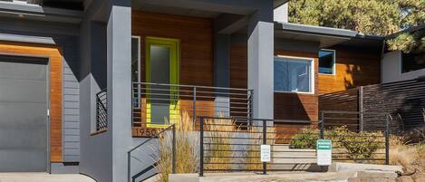 A modern two-story house with a grey exterior, a bright green door, and a small front porch with steps leading to the entrance.