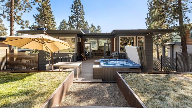 A modern outdoor patio with a hot tub, wooden deck, and a large umbrella. - New! Modern Bend Retreat | Views | Hot Tub | Fenced Yard (Bend)