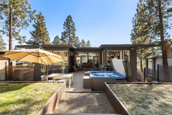 Eine moderne Terrassengrundstück mit Whirlpool, Holzdeck und einem großen Sonnenschirm.