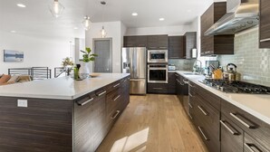 A modern kitchen with dark wood cabinets, stainless steel appliances, and a large island with a white countertop. - New! Modern Bend Retreat | Views | Hot Tub | Fenced Yard (Bend)
