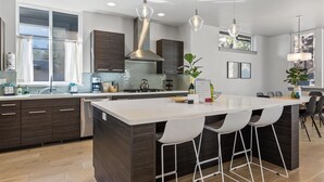 A modern kitchen with dark wood cabinets, a large island with bar stools, stainless steel appliances, and pendant lighting. - New! Modern Bend Retreat | Views | Hot Tub | Fenced Yard (Bend)