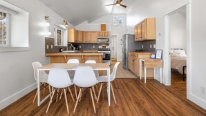Een moderne keuken met houten kastjes, een eettafel met witte stoelen en een plafondventilator.