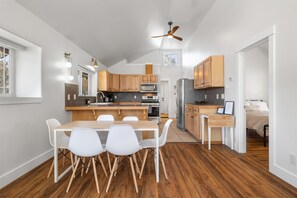 Eine moderne Küche mit Holzausstattung, einem Esstisch mit weißen Stühlen und einem Deckenventilator.