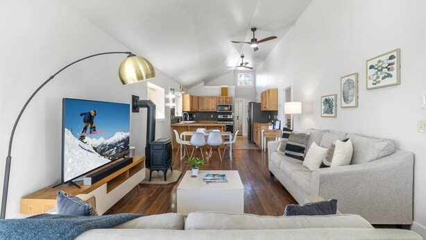 Een moderne woonkamer met een grote flatscreen-tv, een bank, een salontafel en een eethoek met stoelen, met een keuken op de achtergrond.