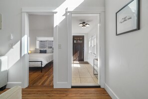 Ein Flur, der zu einem Schlafzimmer führt, mit einem Bett, einem Deckenventilator und einem gerahmten Bild an der Wand.