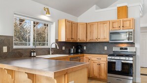 Een moderne keuken met houten kastjes, een groot eiland, roestvrijstalen apparatuur en een raam dat voor natuurlijk licht zorgt.