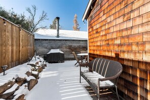 Eine überdachte Terrasse mit Korbstuhl, Tisch, Grill und Holzzaun.