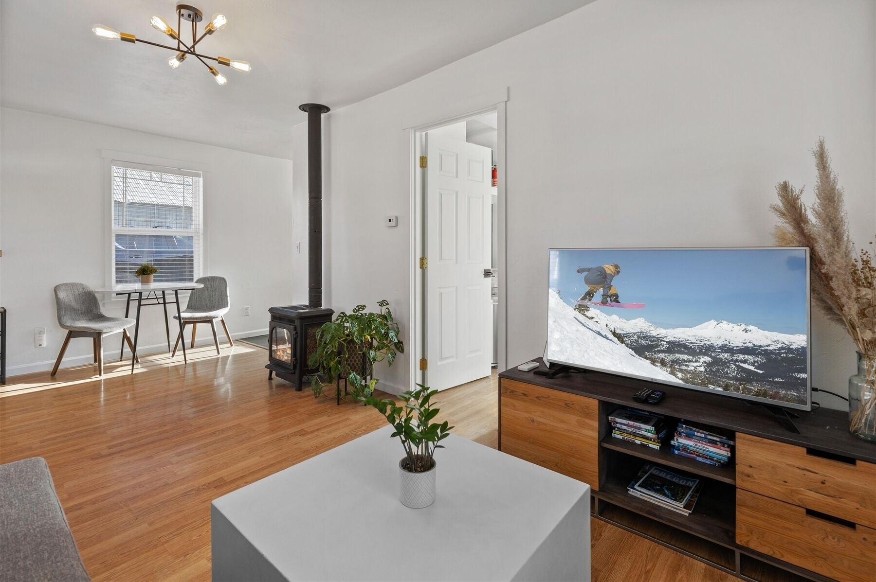 A modern living room with a large flat-screen TV, a wooden floor, a white coffee table with a plant, and a fireplace.
