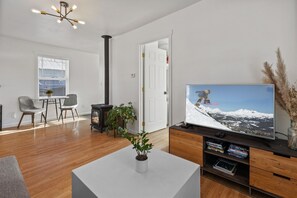 Ein modernes Wohnzimmer mit großem Flachbildfernseher, Holzboden, weißem Couchtisch mit Pflanze und Kamin.