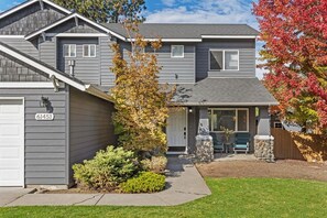 A two-story house with a garage, a stone fireplace, and a well-maintained lawn. - New! Beautiful 5 Bedroom Retreat | Hot Tub | Backyard (Bend)