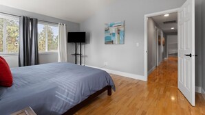 Ein Schlafzimmer mit Bett, Fernseher, einem Gemälde und einem Flur zu einem weiteren Raum.