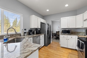 A modern kitchen with white cabinets, stainless steel appliances, and a granite countertop. - New! Beautiful 5 Bedroom Retreat | Hot Tub | Backyard (Bend)