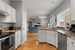 A modern kitchen with white cabinets, granite countertops, and a central island. - New! Beautiful 5 Bedroom Retreat | Hot Tub | Backyard (Bend)