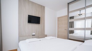 Habitación de hotel con cama, televisor montado en la pared, armario de madera y espejo con literas.