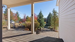 Una terraza cubierta de madera con vista a un jardín ajardinado y una casa al fondo.