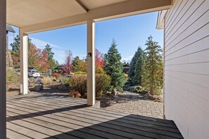 Eine überdachte Holzterrasse mit Blick auf einen angelegten Garten und ein Haus im Hintergrund.