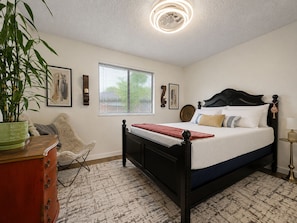 Quarto com cama, uma cadeira, cômoda, janela e luminária no teto.